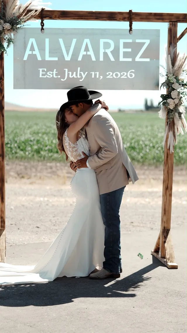 A couple embracing beneath a wooden arch and their wedding-date sign