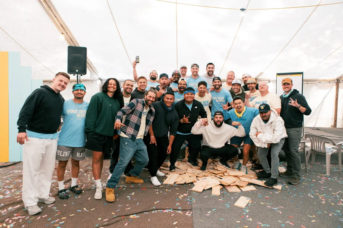 A company team crowded together for a group photo under a white event tent, most in matching branded t-shirts, confetti across the floor