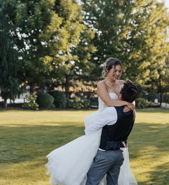 Groom lifting the bride off her feet on a lawn