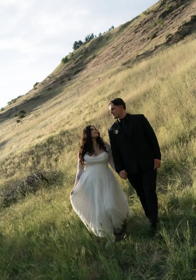Newlyweds walking hand in hand through golden hillside grass