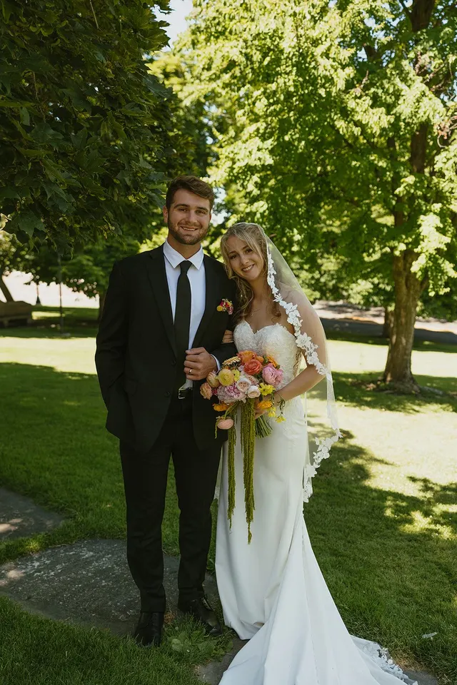 Bride and groom standing together in a park with a colorful bouquet