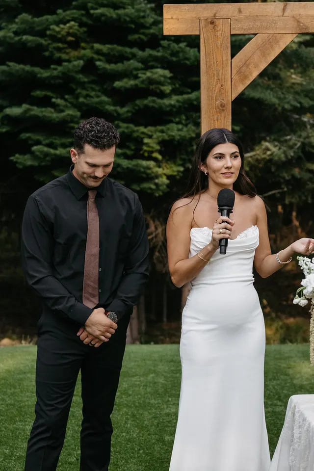 A bride and groom sharing a wireless microphone as they speak to their guests