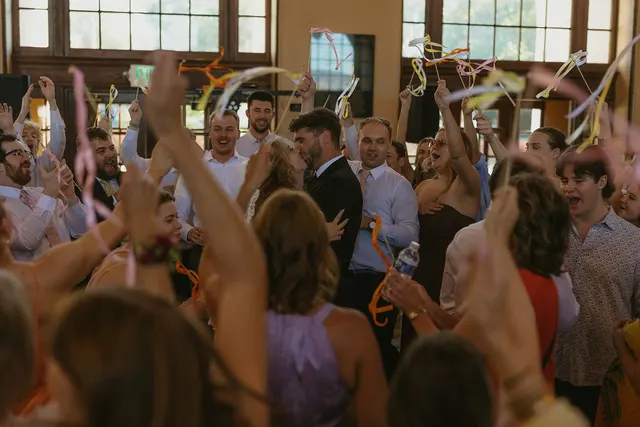 A full hall of wedding guests with their hands up, cheering