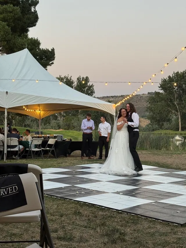 A first dance on a checkered dance floor under a tent at sunset