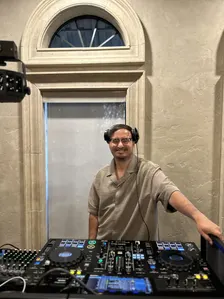 DJ Manny smiling behind his controller in headphones at an indoor venue