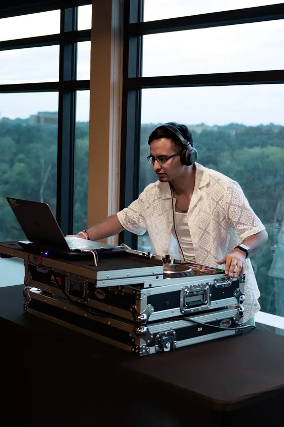 DJ Manny mixing at a booth in front of floor-to-ceiling windows overlooking the hills